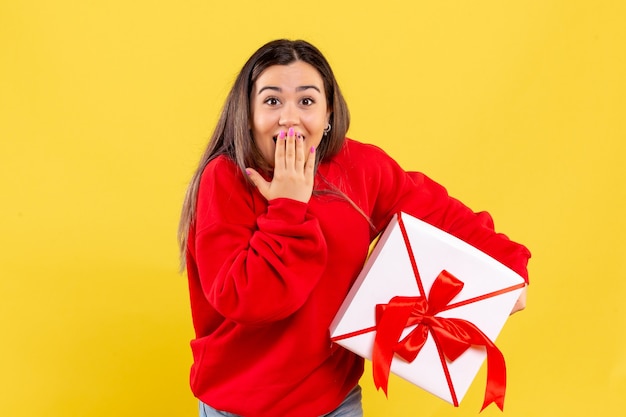 Free photo front view of young woman holding xmas gift on yellow wall