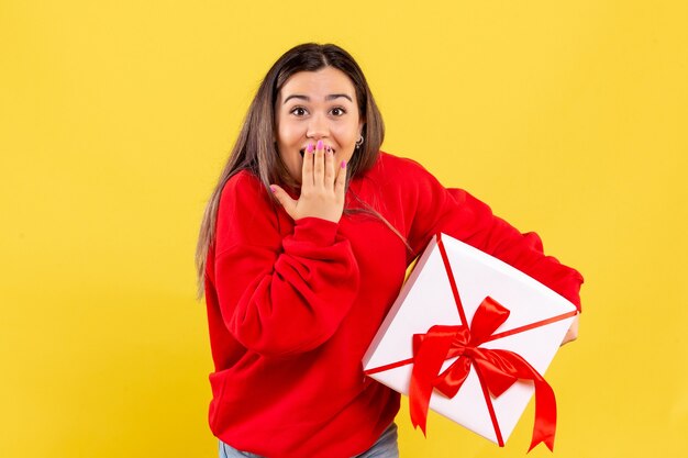 Front view of young woman holding xmas gift on yellow wall