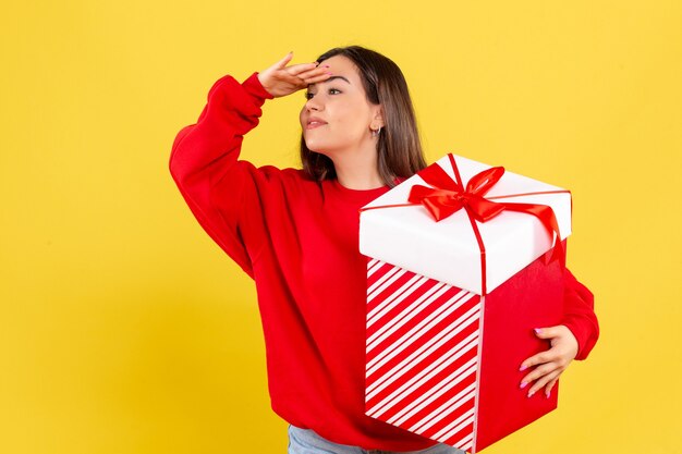 Front view of young woman holding xmas gift on yellow wall