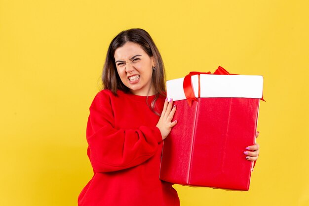 Front view of young woman holding xmas gift on yellow wall