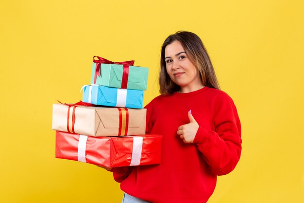 Front view young woman holding xmas gifts on yellow background