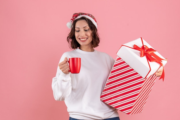 Front view of young woman holding xmas present and cup of tea on a pink wall