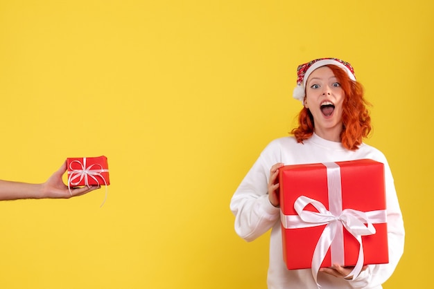 Front view of young woman holding xmas present on yellow wall