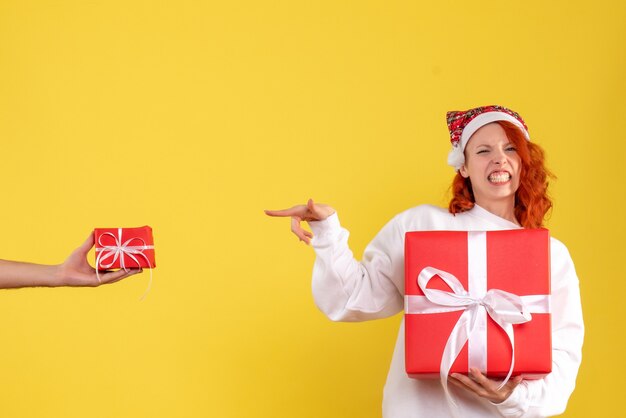 Front view of young woman holding xmas present on yellow wall