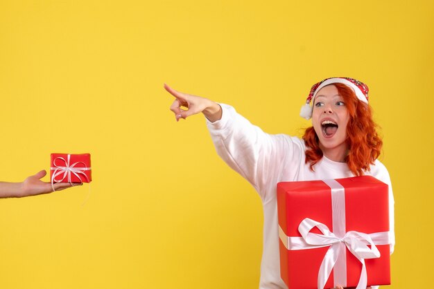 Front view of young woman holding xmas present on yellow wall