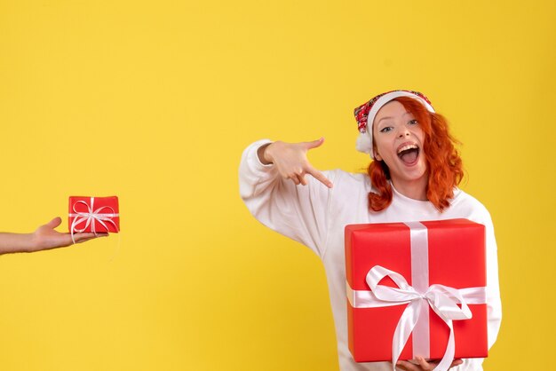 Front view of young woman holding xmas present on yellow wall