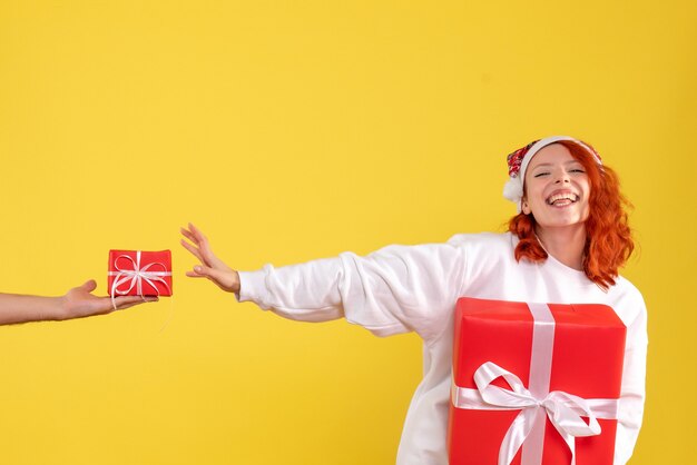 Front view of young woman holding xmas present on yellow wall