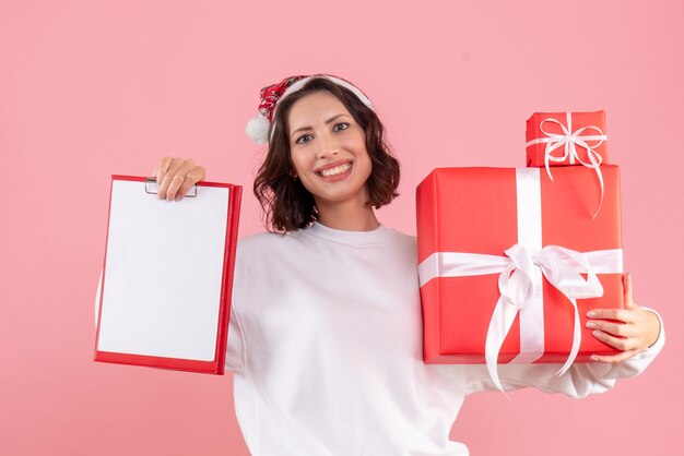 Front view of young woman holding xmas presents on a pink wall