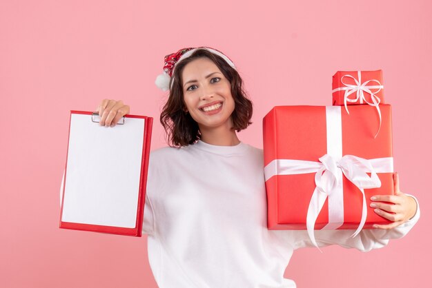 Вид спереди молодой женщины, держащей рождественские подарки на розовой стене
