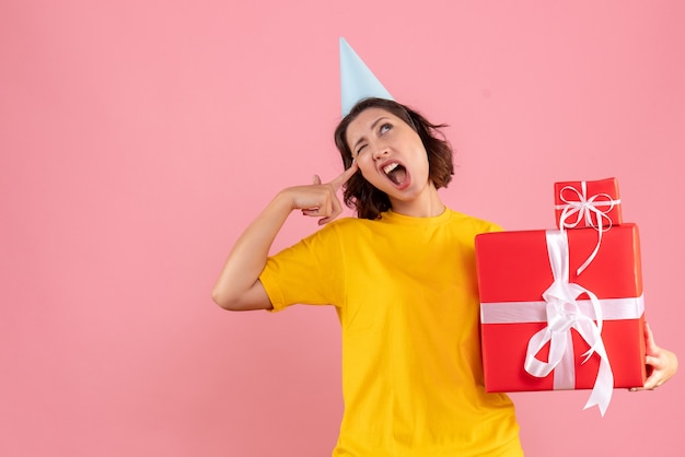 Foto gratuita vista frontale della giovane donna che tiene i regali di natale sulla parete rosa