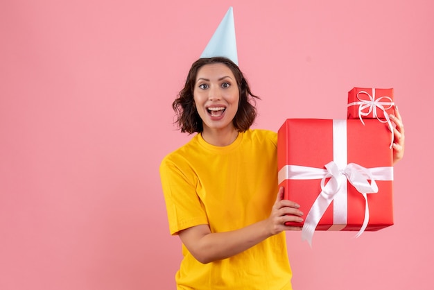 Front view of young woman holding xmas presents on pink wall