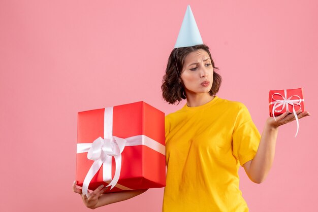 Front view of young woman holding xmas presents on pink wall