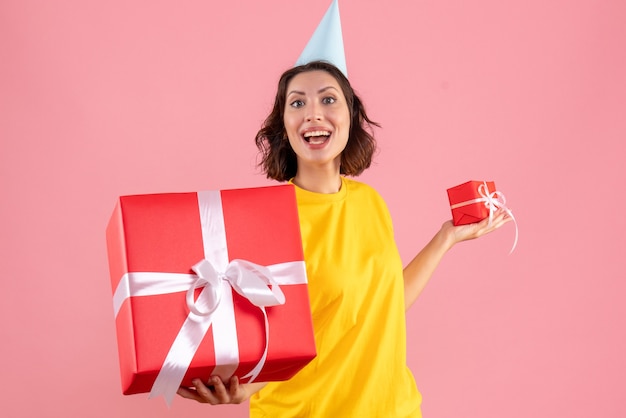 Front view of young woman holding xmas presents on pink wall