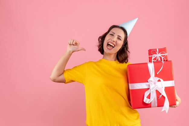 Front view of young woman holding xmas presents on the pink wall