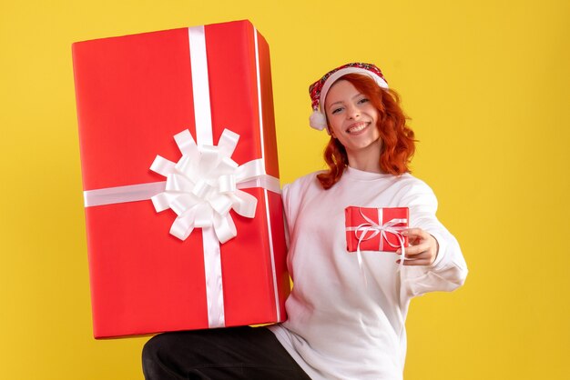 Front view of young woman holding xmas presents on yellow wall