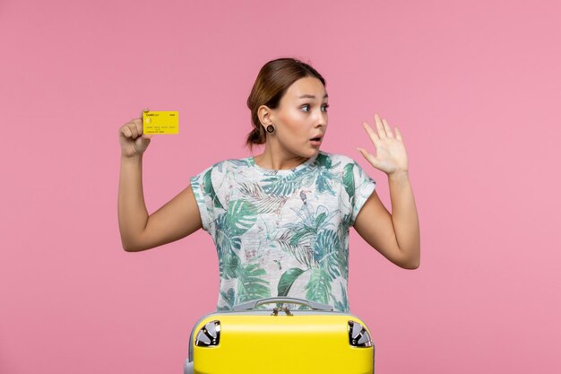 Front view of young woman holding yellow bank card on light pink wall