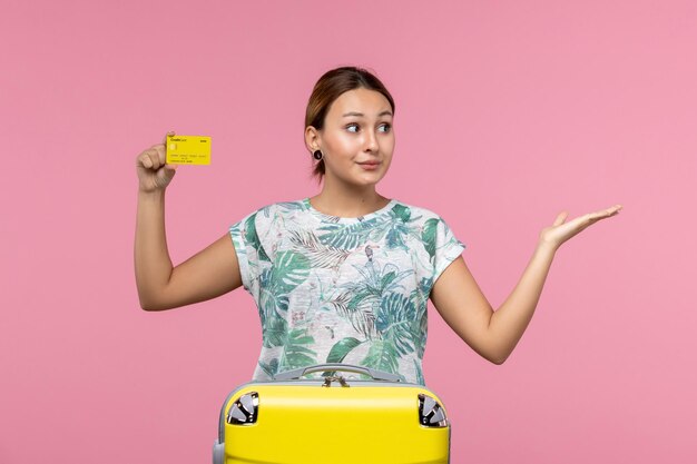 Front view of young woman holding yellow bank card on a pink wall