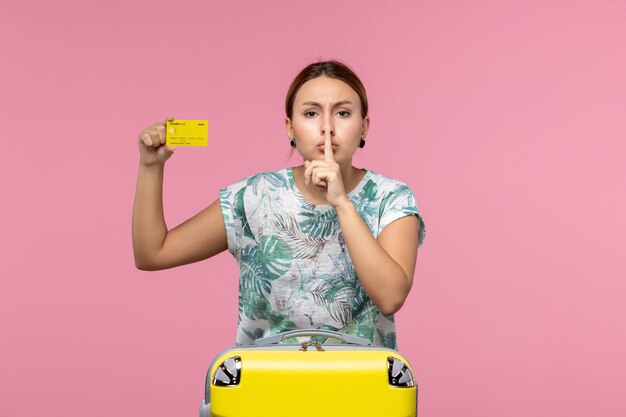 Вид спереди молодой женщины, держащей желтую банковскую карту на розовой стене