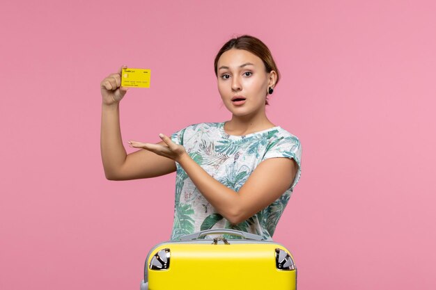 Front view of young woman holding yellow bank card on pink wall