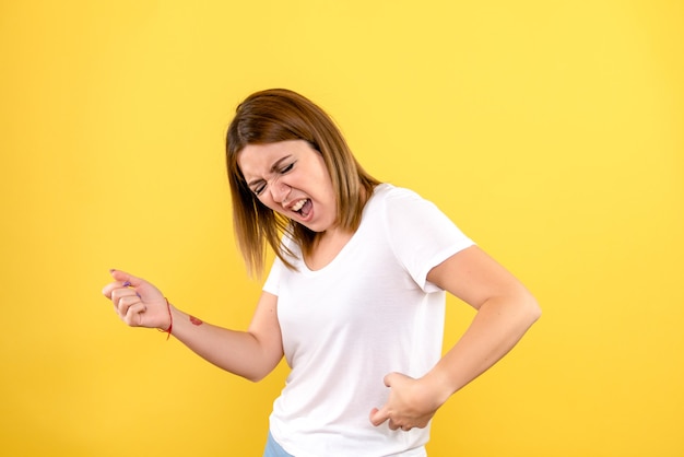 Front view of young woman imitating guitar play on yellow wall