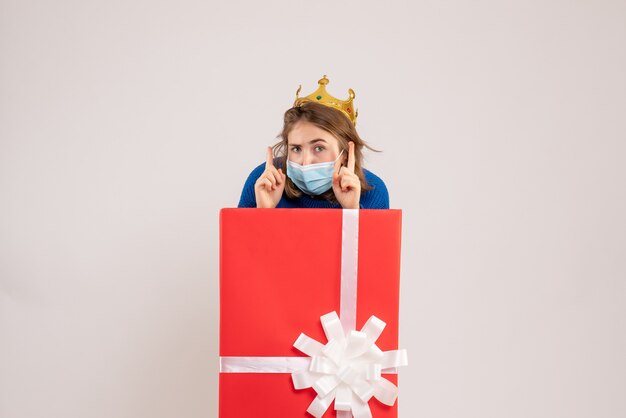 Front view of young woman inside present box in mask on a white wall