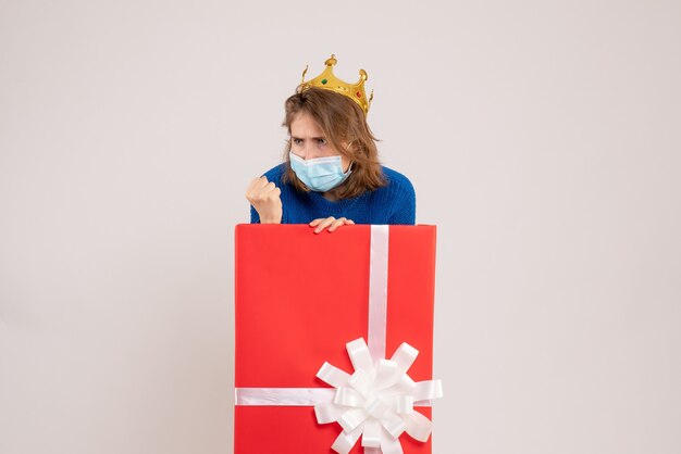 Front view of young woman inside present box in mask on a white wall