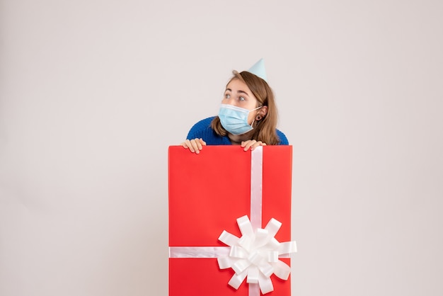 Front view of young woman inside present box in mask on a white wall