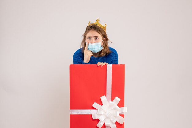 Front view of young woman inside present box in mask on white wall