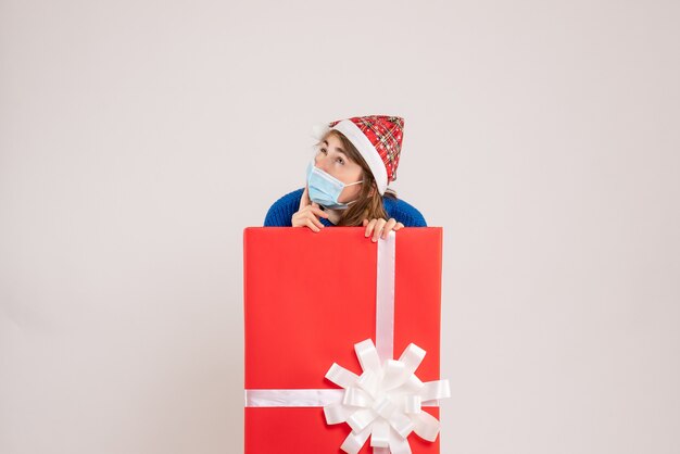 Front view of young woman inside present box in mask on white wall