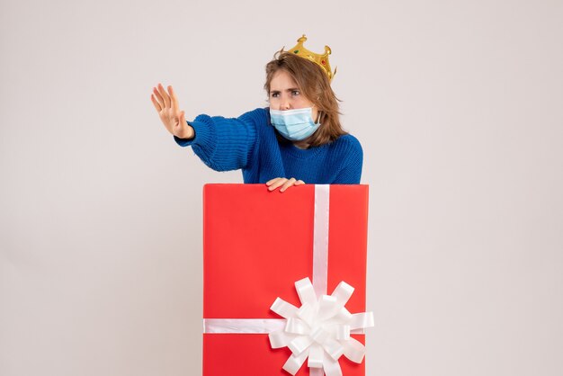 Front view of young woman inside present box in mask on white wall