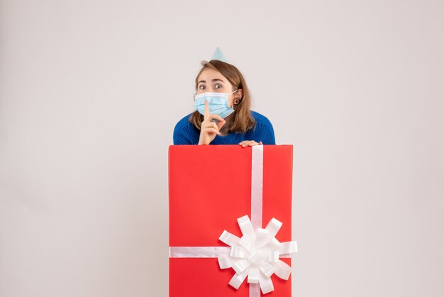Front view of young woman inside present box in mask on white wall