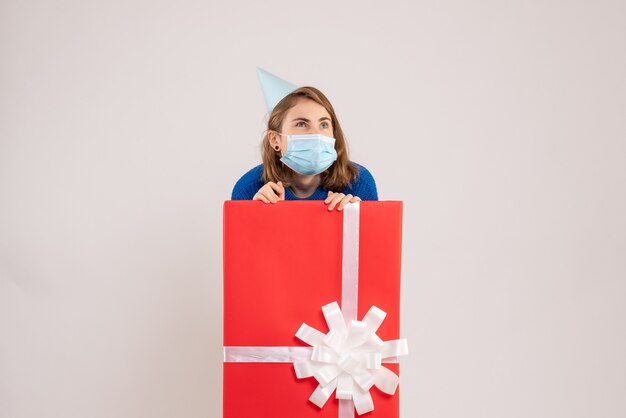 Front view of young woman inside present box in mask on white wall