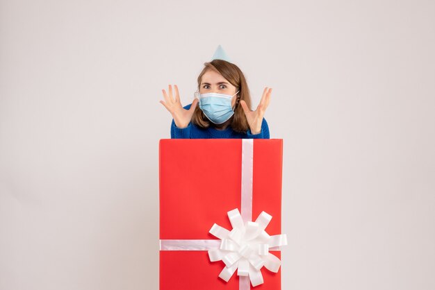 Front view of young woman inside present box in mask on white wall