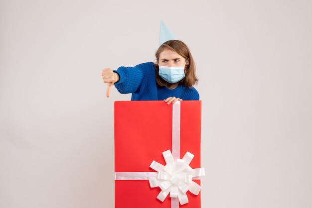 Front view of young woman inside present box in mask on white wall