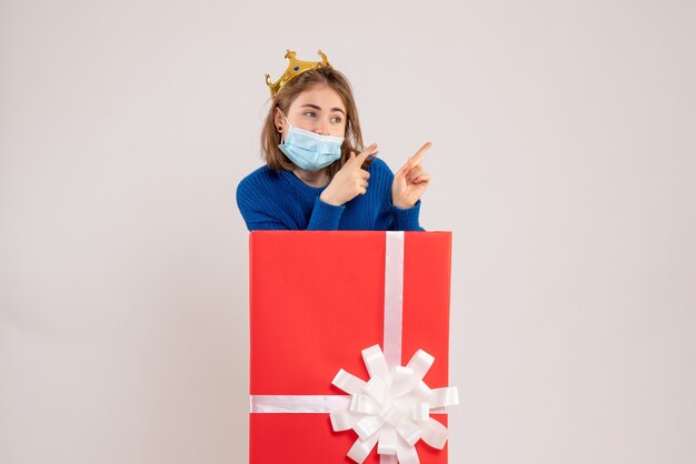 白い壁の上の滅菌マスクのプレゼントボックス内の若い女性の正面図