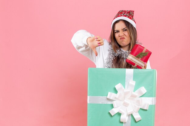 Front view of young woman inside present holding another present displeased on pink wall