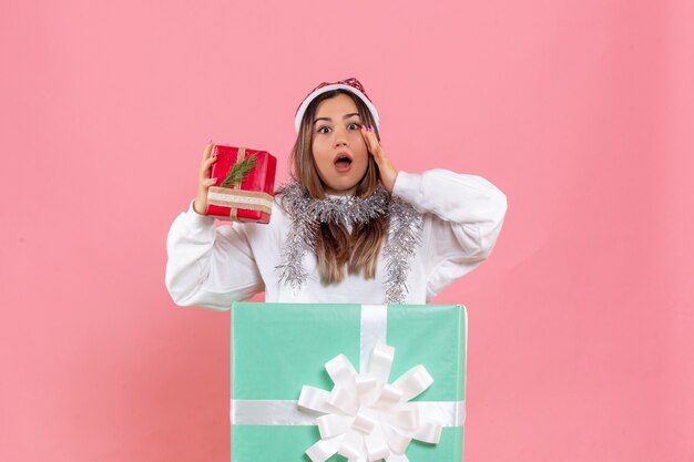 Front view of young woman inside present holding another present on the pink wall