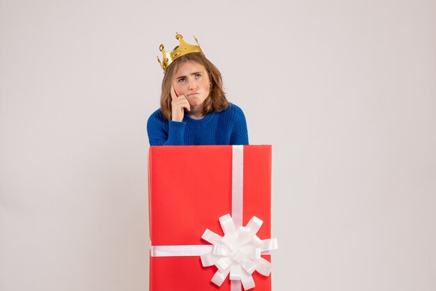Front view of young woman inside red present box thinking on white wall