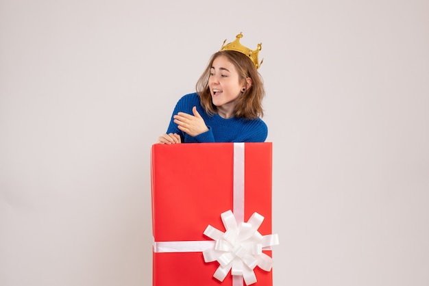 Вид спереди молодой женщины в красной подарочной коробке на белой стене