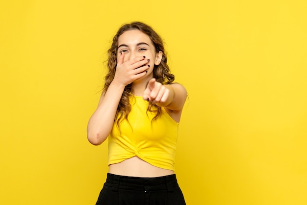 Front view of young woman laughing on yellow wall