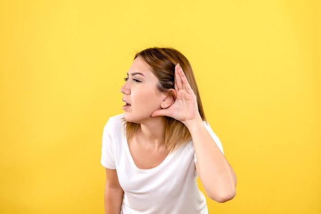 Front view of young woman listening on the yellow wall