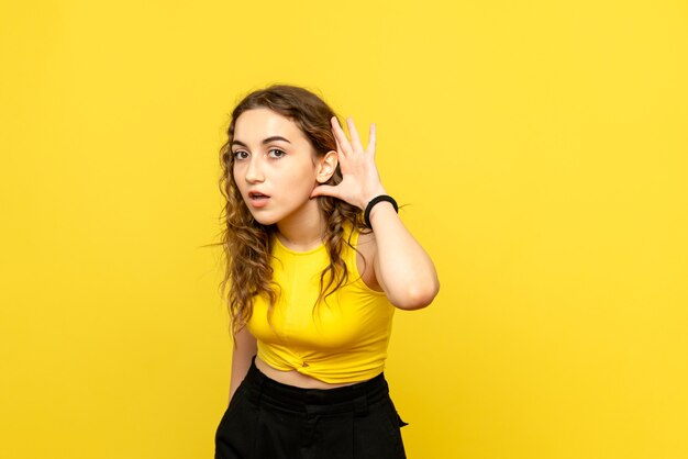Front view of young woman listening on yellow wall