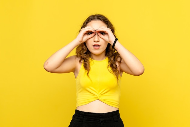 Free photo front view of young woman looking through eyes on yellow wall