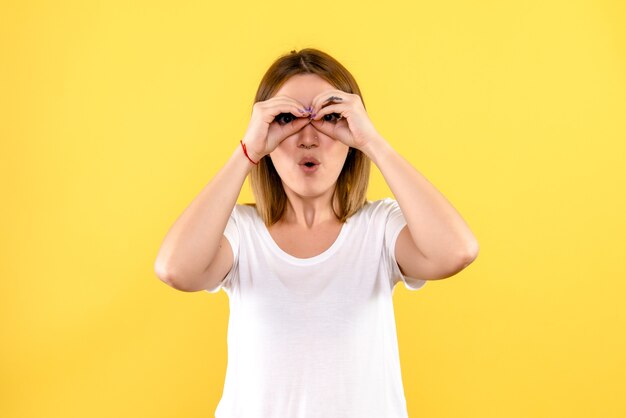 Front view of young woman looking through fingers on yellow wall