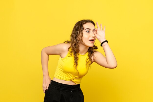Front view of young woman looking through her eyes on yellow wall