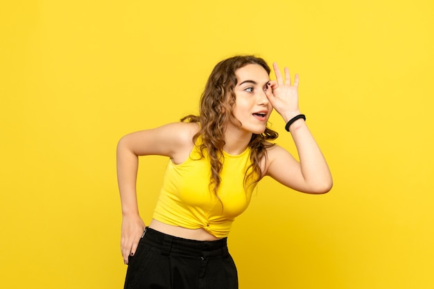 Front view of young woman looking through her eyes on yellow wall