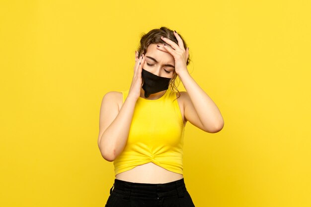 Front view of young woman in mask on light yellow wall