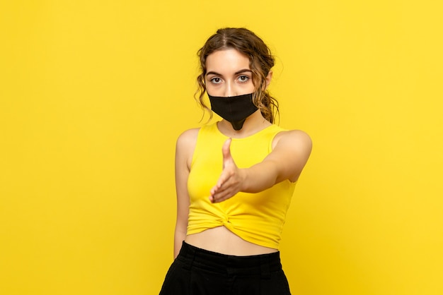 Front view of young woman in mask shaking hands on yellow wall