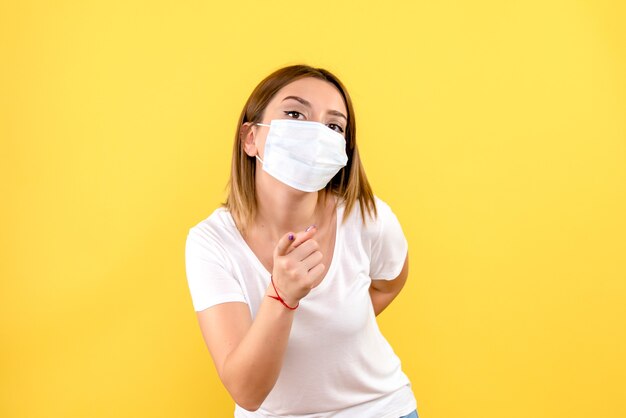 Front view of young woman in mask on yellow wall