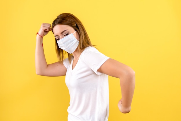 Front view of young woman in mask on yellow wall